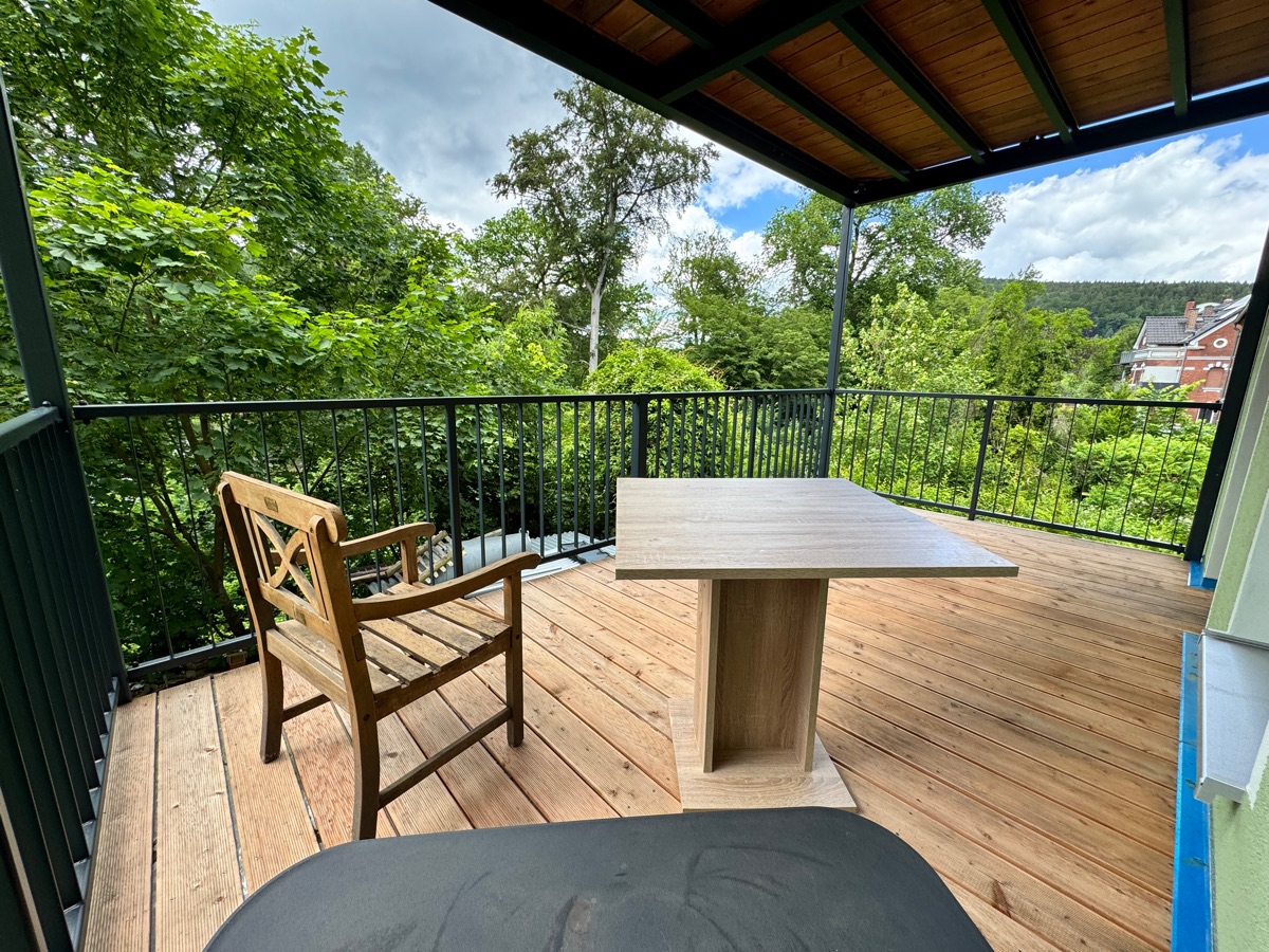 Überdachter Balkon der Ferienwohnung mit Holzdielen, Sitzplatz und Blick ins Grüne