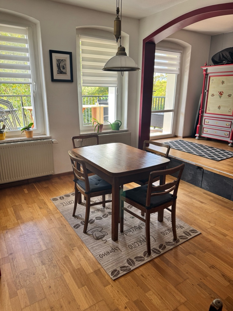 Dining area with wooden table, four chairs, parquet floor and painted farmhouse cabinet, with window and balcony door behind