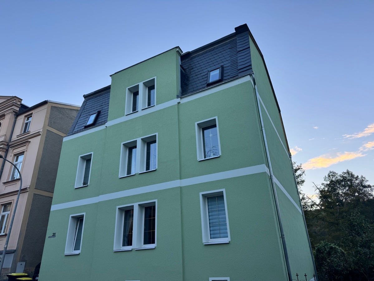 Green rendered house at Leonhardtstraße 31 in Greiz with slate roof in the evening, with the trees at the edge of the park on the right