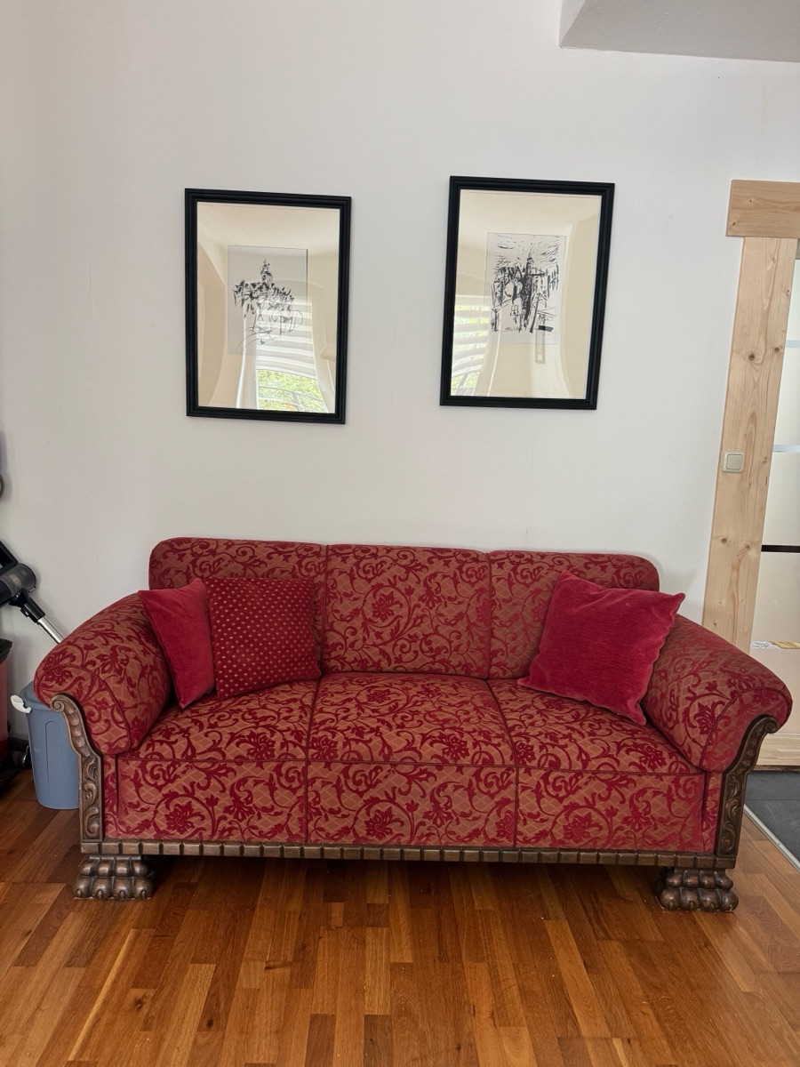 Red upholstered sofa beneath two framed original prints by regional artists