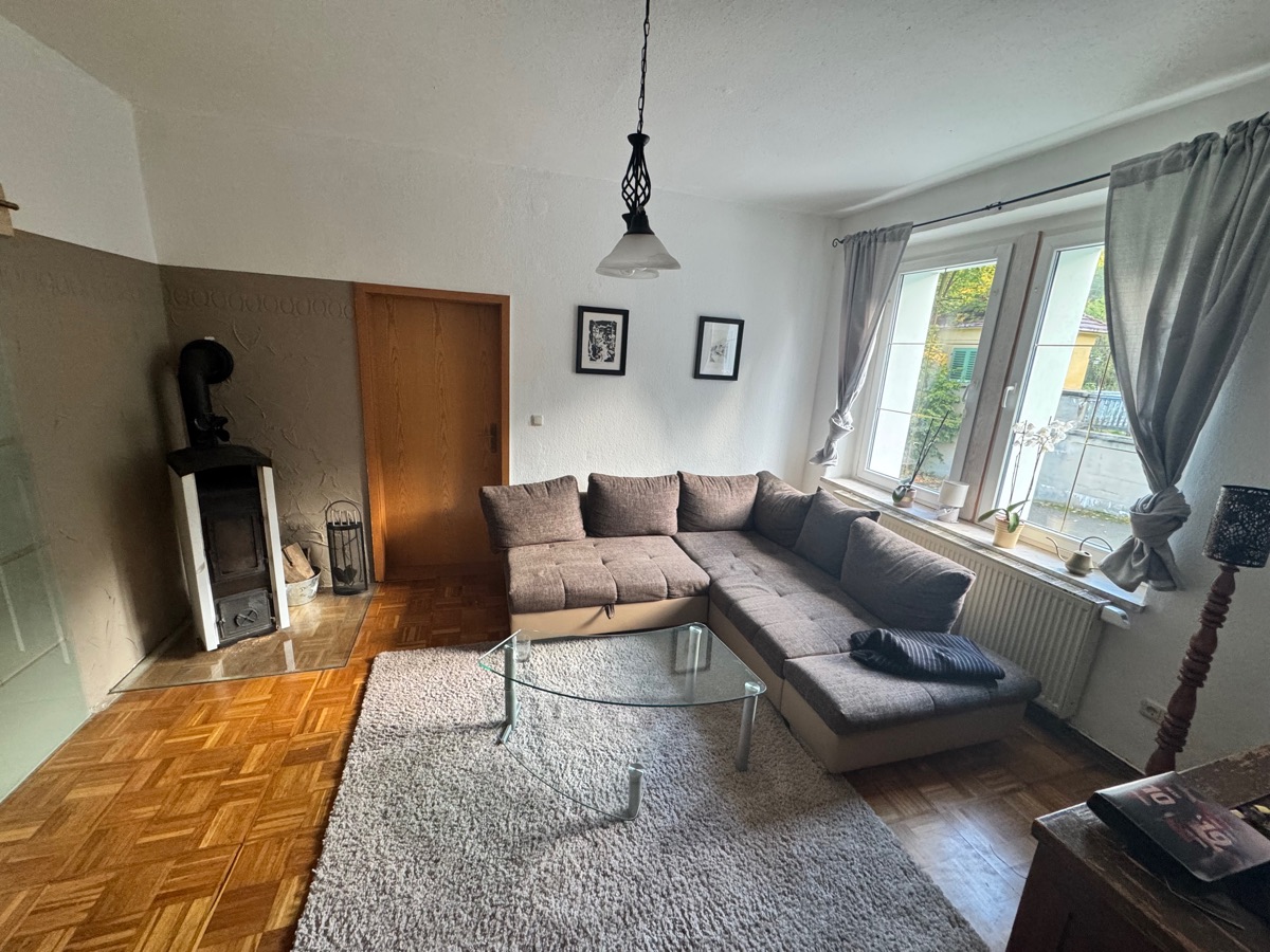 Living room with corner sofa, glass table, rug, parquet floor and wood-burning stove